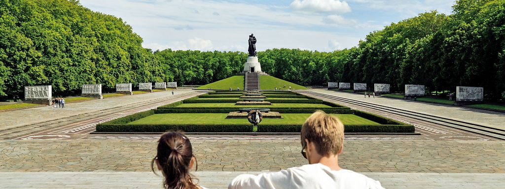 Zwei Personen sitzend, im Hintergrund das Sowjetisches Ehrenmal Treptower Park in Berlin