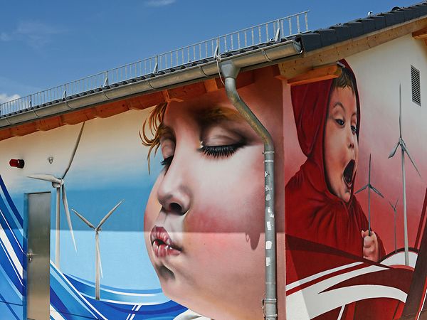 Graffiti an einer Häuserwand zeigt Kinder die Windräder anpusten