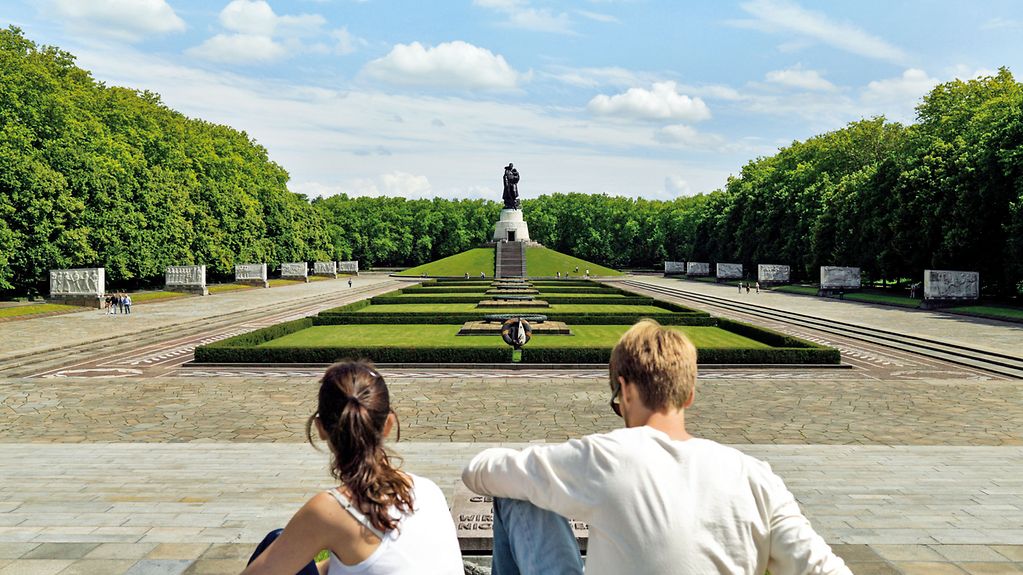 Zwei Personen sitzend, im Hintergrund das Sowjetisches Ehrenmal Treptower Park in Berlin