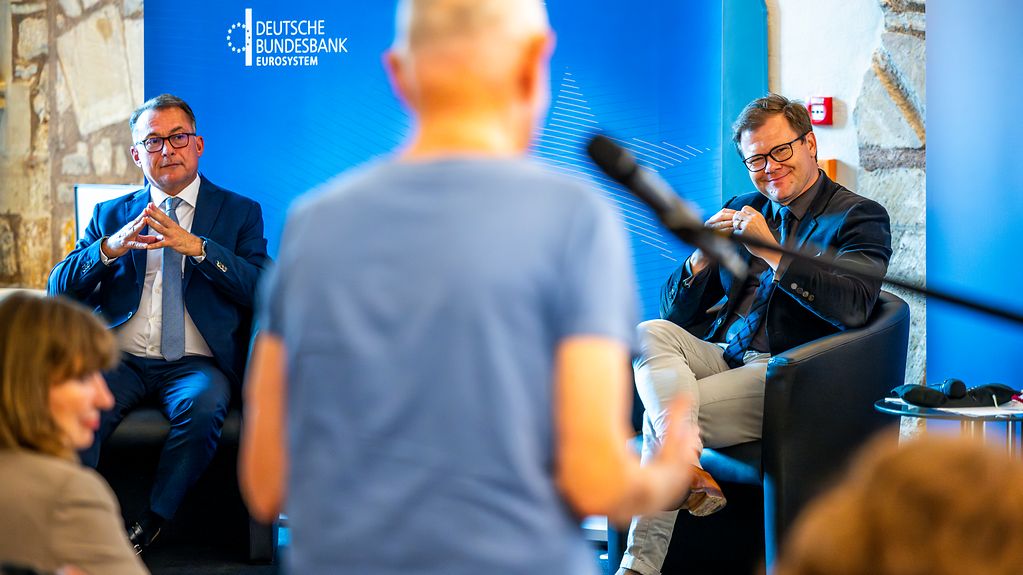 Bundesbankpräsident Joachim Nagel und Staatsminister Carsten Schneider sitzen auf der Bühne und warten auf die Frage eines Mannes aus dem Publikum